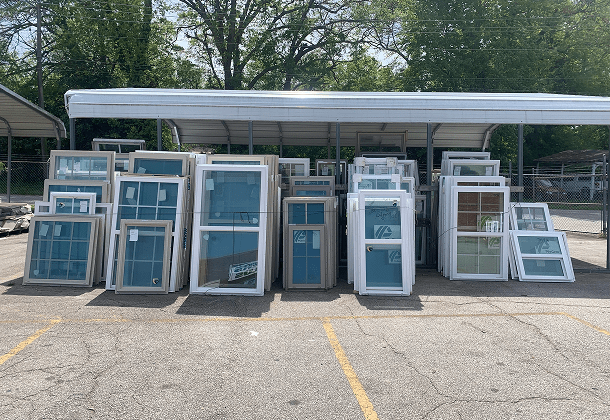Old wooden windows for sale in various sizes arranged in rows at outdoor salvage yard
