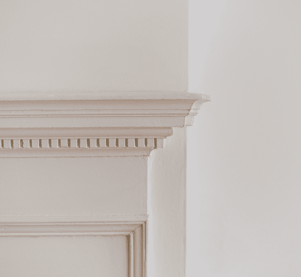 Elegant white fireplace mantel with decorative carved details against a plain light-colored wall